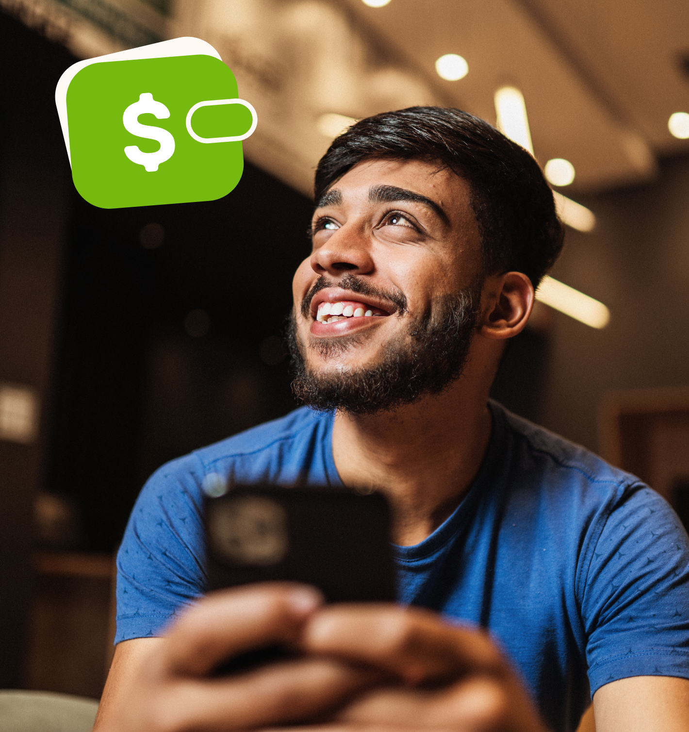 Homem jovem, sorrindo e utilizando um telefone celular em um ambiente de trabalho.